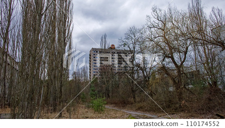 An old apartment building looms behind a forested area, under an overcast sky. 110174552