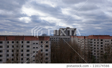 The image shows aged apartments with a backdrop of a dramatic cloudy sky and leafless trees. 110174566