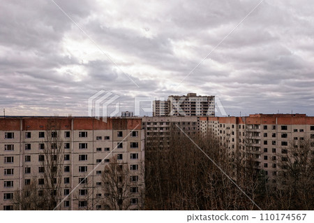 Grey buildings with many windows are surrounded by barren trees under a cloud-filled sky. 110174567