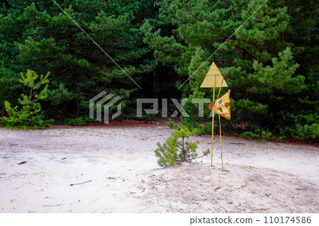 A yellow and black warning sign in a forest, trees. The sign is attached to a post and has trees in the background. Radiation pollution sign near trees in the Chernobyl exclusion zone. A yellow and black warning sign in a forest, trees. The sign is attached to a post and has trees in the background. Radiation pollution sign near trees in the Chernobyl exclusion zone. 110174586