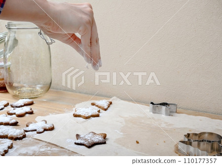 A woman's hand sprinkles white flour on a cookie while preparing a dessert in a home kitchen. 110177357