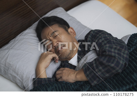 A man in his mid-50s sleeps with a painful expression on his face. 110178275