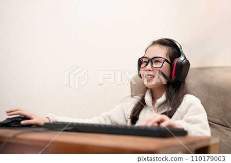 A girl wearing headphones and operating a computer A girl wearing headphones and operating a computer 110179003
