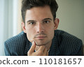 Close-up of young handsome guy in a white shirt, looks seriously and intently at the camera indoor 110181657