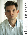 Close-up of young handsome guy in a white shirt, looks seriously and intently at the camera indoor 110181660