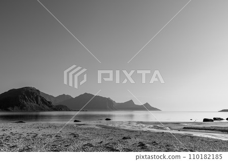 Gentle waters meet a layered mountain skyline at Haukland Beach in grayscale Gentle waters meet a layered mountain skyline at Haukland Beach in grayscale 110182185