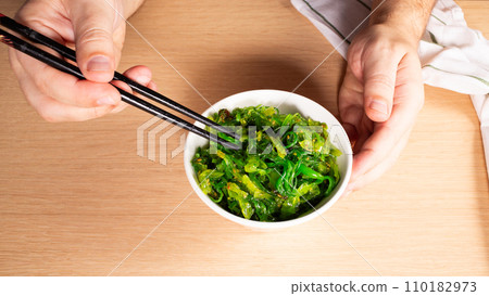 Man holding chopsticks with Japanese seaweed salad over bowl 110182973