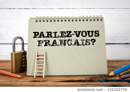 Do you speak French. Written in French. Green notepad on wooden texture table and white background Do you speak French. Written in French. Green notepad on wooden texture table and white background 110183736
