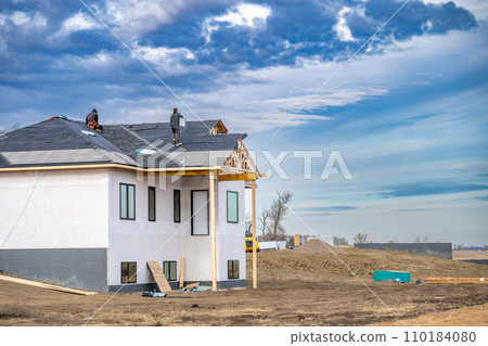 Shingle roof being installed on a two-story walkout new build residential construction house.  110184080