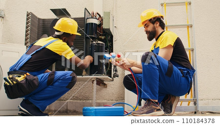African american repairman cleaning condenser internal components of dirt while coworker assembles professional manifold meters to check freon levels in hvac system 110184378