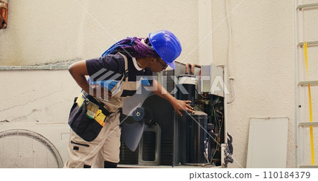 Precise mechanic commissioned for external hvac system routine maintenance, looking for damaged electric components. Skilled african american electrician doing condenser safety check Precise mechanic commissioned for external hvac system routine maintenance, looking for damaged electric components. Skilled african american electrician doing condenser safety check 110184379