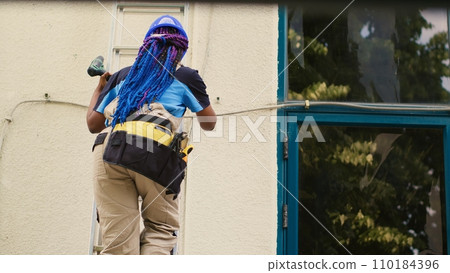 Adept repairman holding electric drill, stepping down from folding ladder after finishing check up on rooftop hvac system. Proficient worker at the end of maintenance assignment 110184396