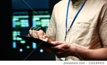 Meticulous technician doing checkup, inputing data on tablet of needed fixes in server hub housing advanced data storage infrastructure supporting critical IT workloads, close up 110184433
