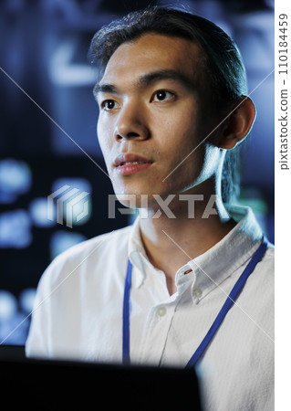 Portrait of technician between server hub clusters providing processing resources for businesses worldwide. Experienced professional fixes data center mainframes tasked with managing massive databases 110184459