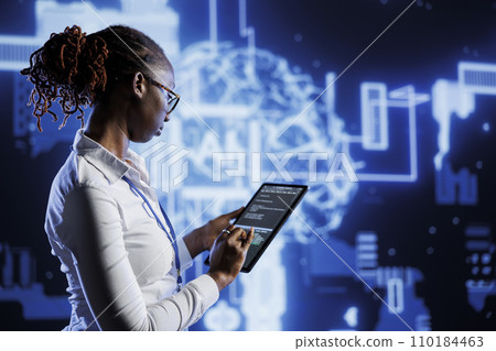Knowledgeable admin updates neural networks made of interconnected nodes, writing intricate lines of code on tablet. High tech establishment employee uses programming to upgrade AI simulation model 110184463