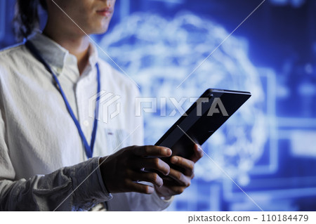 Admin using tablet in server room to maintenance artificial intelligence neural networks simulating human thought processes. High tech establishment worker does checkup on AI systems Admin using tablet in server room to maintenance artificial intelligence neural networks simulating human thought processes. High tech establishment worker does checkup on AI systems 110184479