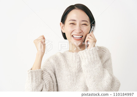 中年婦女一邊用智慧型手機說話一邊握拳，背景是白色 110184997