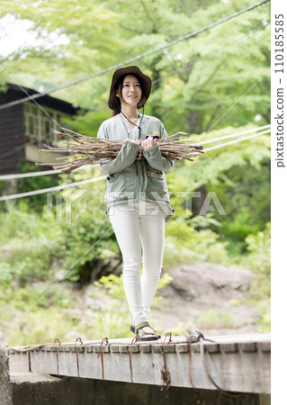 一名婦女在營地裡搬運木柴（樹枝） 110185585