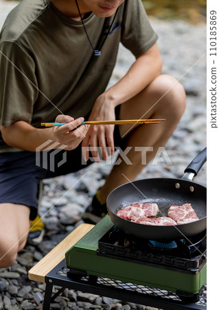 A man grilling pork at a camp gas stove 110185869