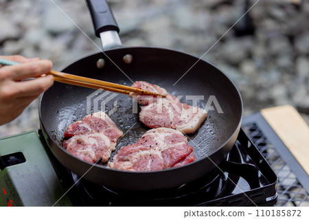 A man grilling pork at a camp gas stove 110185872