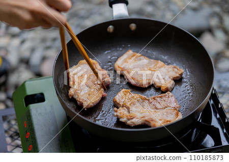 A man grilling pork at a camp gas stove 110185873