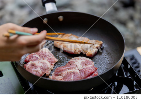 A man grilling pork at a camp gas stove 110186003