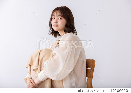 A woman in a dress sitting on her knees on a chair 110186630