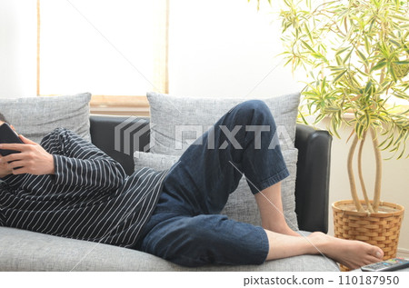 A man lying on the sofa and operating a smartphone. 110187950