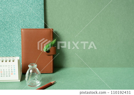 Diary notebook, calendar, vase of plant, colored pencil on desk. green wall background. planning office supply Diary notebook, calendar, vase of plant, colored pencil on desk. green wall background. planning office supply 110192431