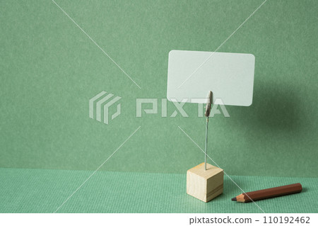 Memo pad with holder and colored pencil on desk. green wall background. copy space Memo pad with holder and colored pencil on desk. green wall background. copy space 110192462