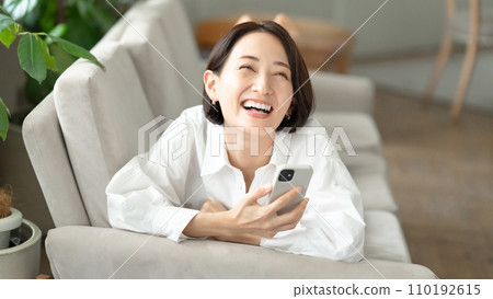 A woman lying on the sofa and operating a smartphone A woman lying on the sofa and operating a smartphone 110192615