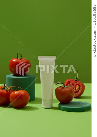 Cosmetic tube with empty label and some fresh tomatoes decorated over green background. Natural beauty blank label for branding mock-up concept 110198689