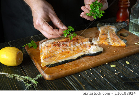 We prepare fresh red fish in the restaurant kitchen before salting with aromatic spices. Chef hand adding parsley to fish steak We prepare fresh red fish in the restaurant kitchen before salting with aromatic spices. Chef hand adding parsley to fish steak 110198924