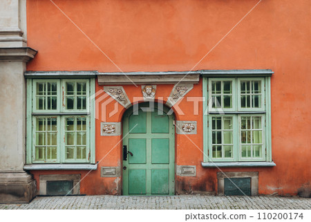 A vintage red house with old green door and two windows. Ancient wooden door in old building wall. 110200174