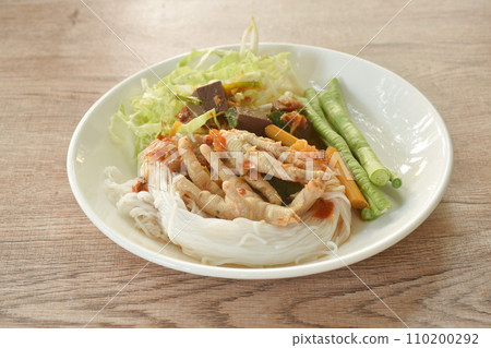 rice noodles with spicy chicken curry sauce and fresh vegetable on plate 110200292
