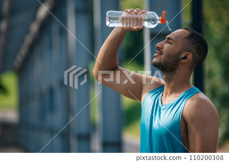 Young dark-skinned athlete pouring some refreshing water on himself after workout Young dark-skinned athlete pouring some refreshing water on himself after workout 110200308