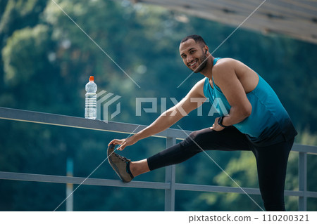 Dark-haired man in sportswear exercising and stretching his legs Dark-haired man in sportswear exercising and stretching his legs 110200321