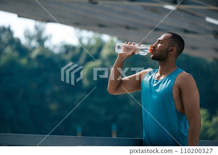 Well-built handsome sportsman drinking water after workout 110200327