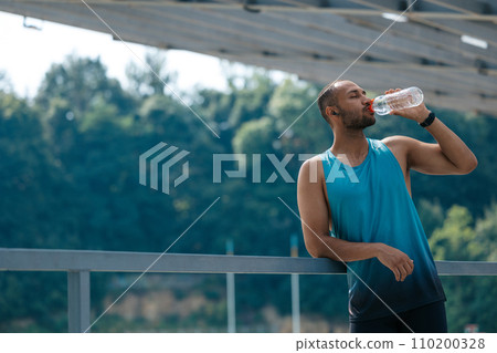 Well-built handsome sportsman drinking water after workout 110200328