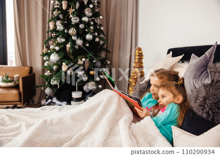 Two sweet girls lying in bed and reading fairy-tales 110200934