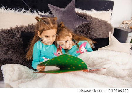 Two sweet girls lying in bed and reading fairy-tales Two sweet girls lying in bed and reading fairy-tales 110200935