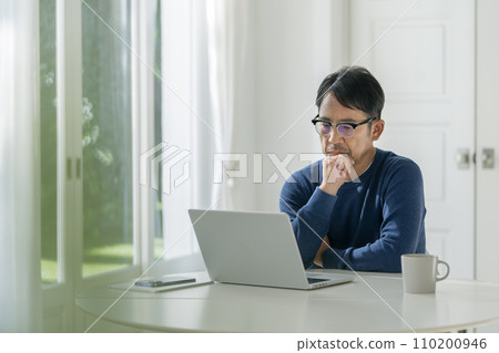 A man in his mid-50s thinking in front of a laptop 110200946