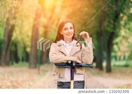 Young woman riding an electric scooter in an autumn park. Green transport, traffic jam problems. Young woman riding an electric scooter in an autumn park. Green transport, traffic jam problems. 110202309