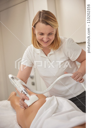 body shaping, roller massage, Endermologie. Professional beauty clinic, young woman doing beauty services, body shaping, masseur giving vacuum roller massage to client, figure correction body shaping, roller massage, Endermologie. Professional beauty clinic, young woman doing beauty services, body shaping, masseur giving vacuum roller massage to client, figure correction 110202856