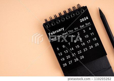 February 2024 Black spiral desktop calendar and wooden pencil. 110203262
