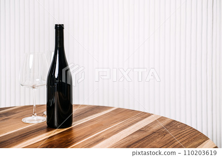 Minimalist Wine Bottle and Glasses on Wooden Table. A simple yet elegant setup of a wine bottle and two glasses on a polished wooden table against a striped background. 110203619
