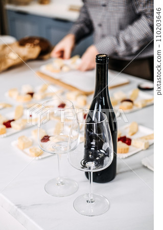 Preparing Appetizers with Wine for a Gathering. Unfocused hands arranging cheese and bread appetizers on a marble counter, with an empty wine bottle and glasses in the foreground. 110203646