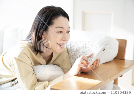 沙發上看著智慧型手機時微笑的女人 110204329