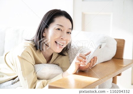 微笑的女人在沙發上拿著智慧型手機 110204332