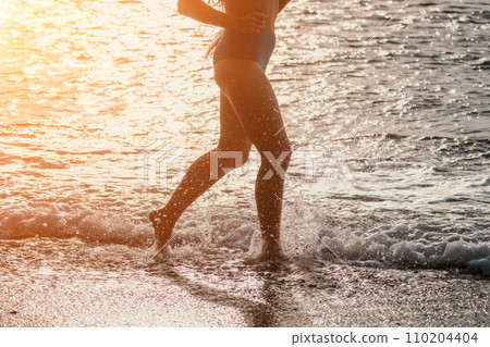 Running woman on a summer beach. A woman jogging on the beach at sunrise, with the soft light of the morning sun illuminating the sand and sea, evoking a sense of renewal, energy and health. Running woman on a summer beach. A woman jogging on the beach at sunrise, with the soft light of the morning sun illuminating the sand and sea, evoking a sense of renewal, energy and health. 110204404